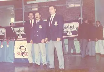 Árbitros de karatê uniformizados em campeonato, ao lado do banner da S.U.K.O.